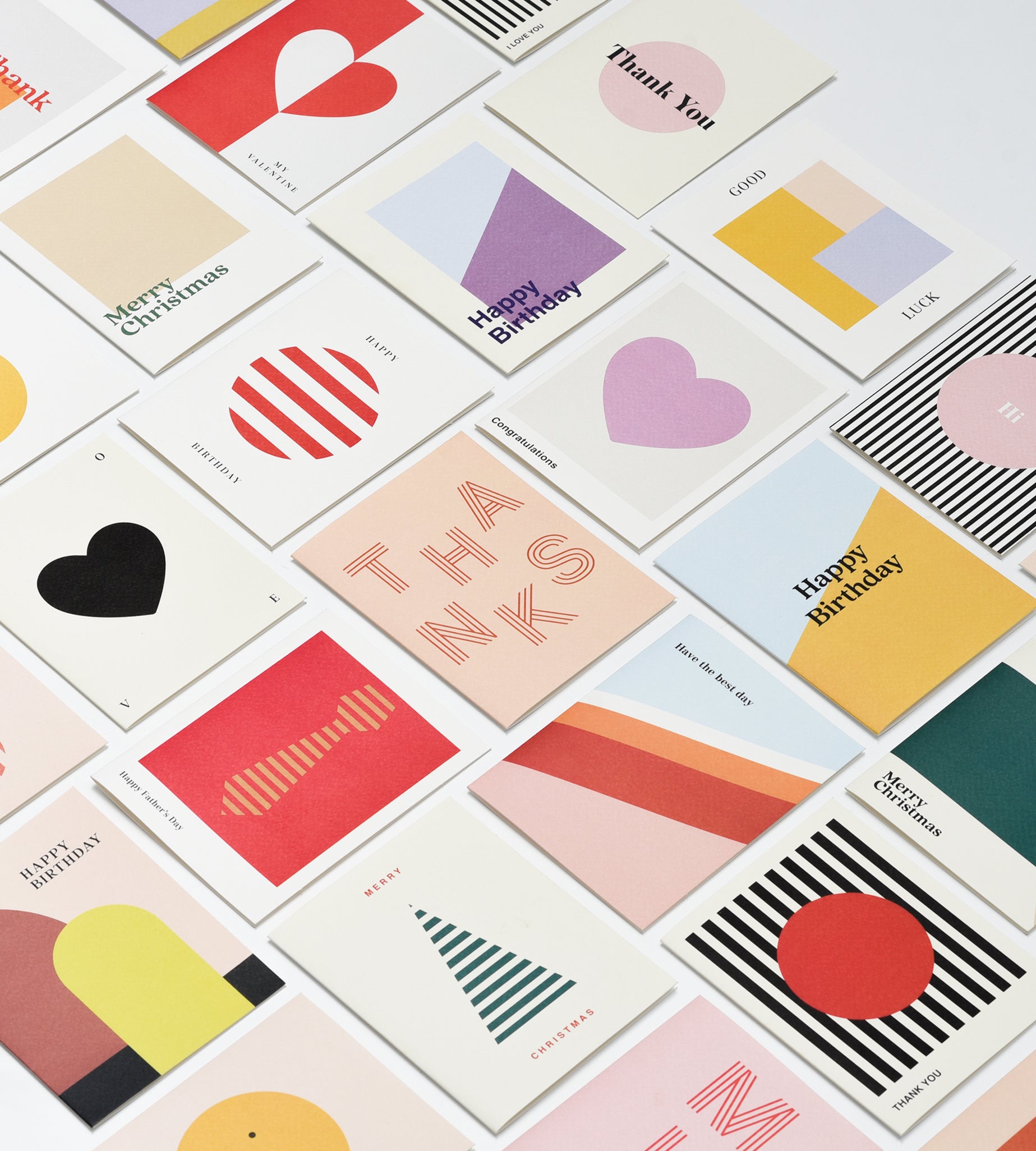 A flat-lay arrangement of multiple minimalist greeting cards with abstract geometric designs in pastel and bright colors on a white background.
